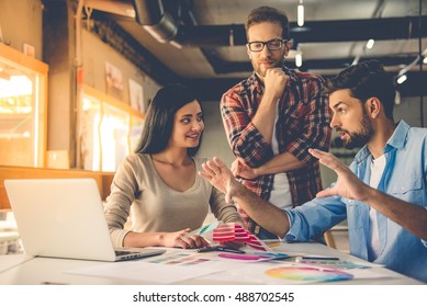 Group of beautiful designers in casual clothes is discussing affairs, choosing colors and smiling while working in studio - Powered by Shutterstock