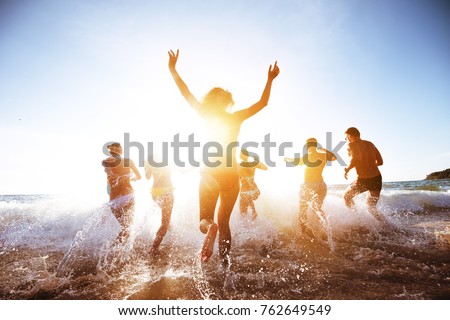 Group of beautiful people having fun, run and jumps at sunset beach
