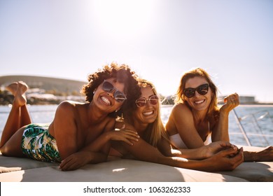 Group of beautiful women relaxing on a yacht deck. Three female friends sunbathing on small boat looking at camera and smiling.