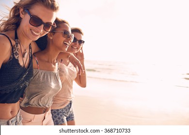 Group of beautiful young women strolling on a beach. Three friends walking on the beach and laughing on a summer day, enjoying vacation.