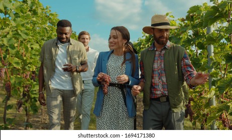 Group of beauty fashion friends walking with farmer on wine tour through gorgeous grapevine garden talking enjoying summertime at vineyard.
