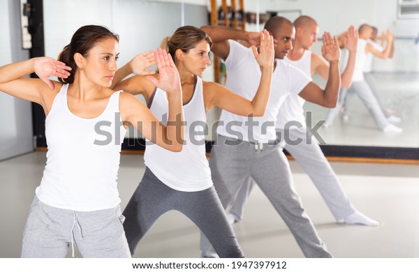 Group of beginners\
mastering martial arts for self defence, synchronously repeating\
basic movements in gym..