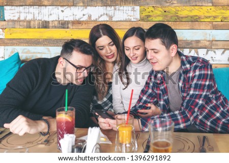 Group of best friends sitting together in pub looking at mobile phone and smiling - Young guy showing something to his friends on smart phone – millennial people connected online at restaurant