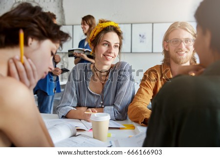 Group of best friends or university students hanging out at coffee shop, talking, having fun, spending nice time together, telling jokes and laughing, sitting at table with textbooks. Selective focus