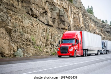 Group of big rigs semi trucks tractors transporting cargo in different semi trailers standing off road in a line near a stone cliff take a break at the pass on top of a mountain range in California