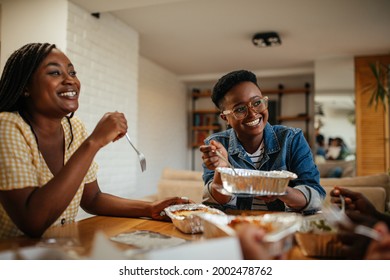 Group of black friends eating takeout food at home. They are chatting and having a relaxing lunch time together