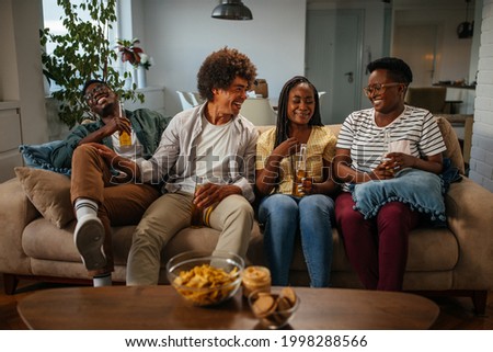 Group of black friends sitting on sofa at home, hanging, holding beer bottles in hands.