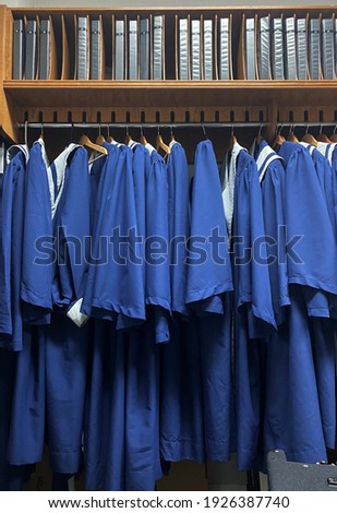 Group of blue choir robes hung up on a rack with the choir books inside a church closet. 