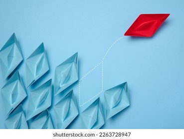 A group of blue paper boats and one red one moving in the opposite direction, the concept of independent personality and breaking away from influence - Shutterstock ID 2263728947