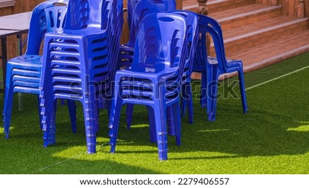 Group of blue plastic chairs and foldable table on green artificial turf outside of building for outdoors event