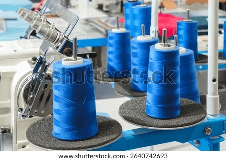 A group of blue and white spools of thread are being made on a machine. The spools are arranged in a row and are of varying sizes