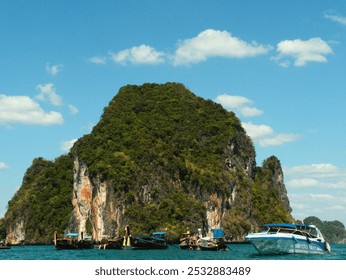 A group of boats are docked on a rocky shore. The boats are of various sizes and colors, including a blue boat. The scene is peaceful and serene, with the boats - Powered by Shutterstock