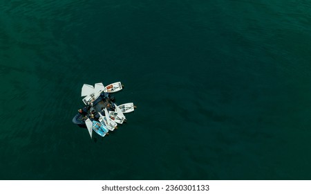 A group of boys and girls, each on top of their optimist boat, surround their instructor who teaches them classes in the middle of the Pacific Ocean. - Powered by Shutterstock