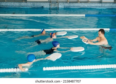 A group of boys and girls train and learn to swim in a modern swimming pool with an instructor. Development of children's sports. Healthy parenting and promotion of children's sports. - Powered by Shutterstock
