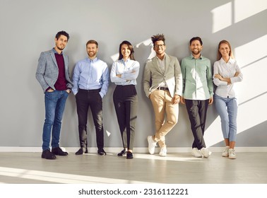 Group of business multiethnic people men and women looking at camera and smiling on gray wall background. Company employees team or group of staff standing in the office confidently and cheerfully.