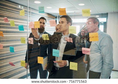 Group of business people brainstorming with sticky notes on glass window