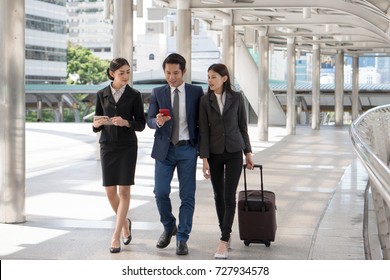 Group Of Business People Checking Flight From Mobile Phone During Walk To Check In At Airport. Boss Sending Staff / Employee To Business Trip Conference.