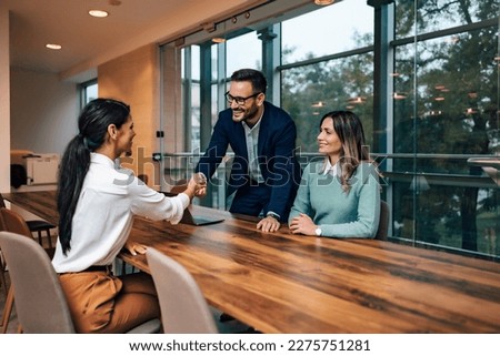 Group of business people closing a deal with a female client, businessman handshake with her, standing in the meeting room.