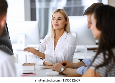 Group of business people discussing questions at meeting. Headshot of blonde businesswoman while smiling to her colleague at office negotiation. Teamwork and cooperation in corporate occupation