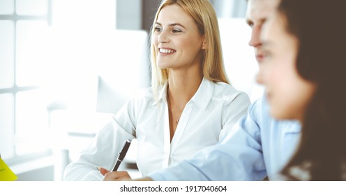 Group of business people discussing questions at meeting. Headshot of blonde businesswoman while smiling to her colleague at office negotiation. Teamwork and cooperation in corporate occupation
