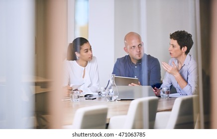 Group Of Business People In Discussions In Modern Office Building Conference Room Shot From Outside The Room Through The Glass Walls.