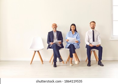 Group Of Business People With Documents In Hand Sitting On Chairs In The Lobby And Waiting For An Interview. Three Candidates Of Different Ages Competing For The Same Position. Staff Employment