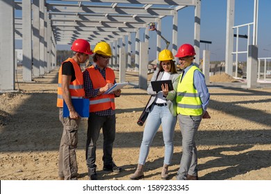 Group Of Business People In Hardhats Discuss A Project On Construction Site. Project Management And Field Crew Meeting On Construction Site. 