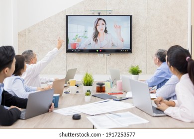 group of business people having conference call meeting in boardroom - asian team leader woman chatting to colleagues using online video chat on tv screen discussing ideas in office