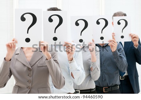 Group of business people hiding their faces behind a question mark sign at office