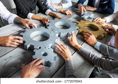 Group of business people joining together silver and golden colored gears on table at workplace
