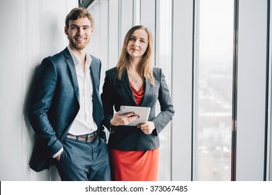 Group Of Business People, A Man In A Suit And A Woman In A Red Dress And Jacket, Holding A Tablet, Winter City Landscape Outside The Window On The Background