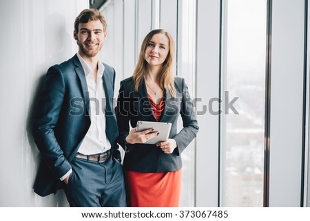 Group of business people, a man in a suit and a woman in a red dress and jacket, holding a tablet, winter city landscape outside the window on the background