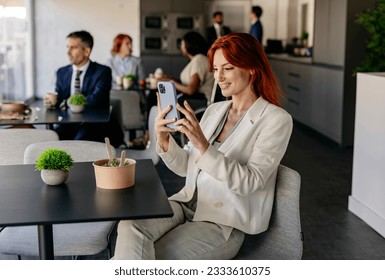 group of business people on break eating in office canteen, redhead young woman making selfie looking at smart phone - Powered by Shutterstock