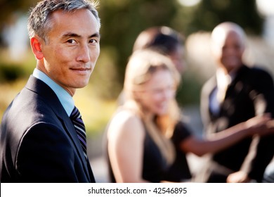 A Group Of Business People Outside - Sharp Focus On Asian Man In Foreground