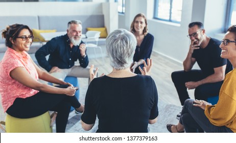 Group Of Business People Sitting In Circle And Discussing In The Office. Mature Woman Talking With Coworkers In A Team Building Session.