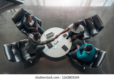 Group Of Business People Sitting And Discussing Statistics During A Sit Down Meeting Taking From Above.