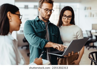 Group of business people using a laptop and having a discussion in an office. Team of business professionals standing together and having a meeting. - Powered by Shutterstock