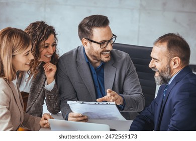 A group of business professionals, displaying a blend of ethnicities, collaborate eagerly around a document. Their professional attire and tools like a laptop suggest an office environment. - Powered by Shutterstock