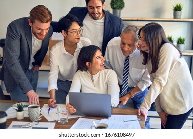Group of business workers smiling happy and confident. One of them sitting and partners standing around. Working together with smile on face looking at the laptop at the office