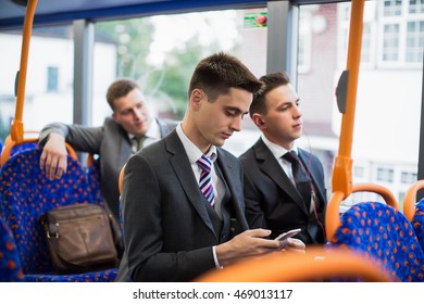 Group Of Businessmen In Suits And Ties Riding The Bus. Serious Face, Look In The Phone, Listen To Music With Headphones.Businessman Using Mobile Phone And Digital Tablet On Bus