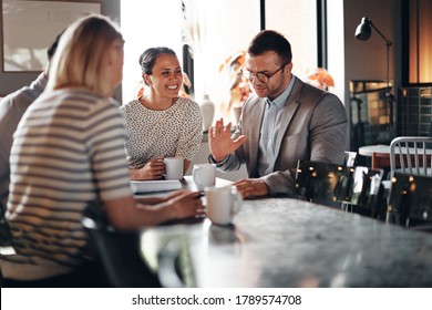 Group of businesspeople talking and laughing together over coffee while sitting in the lounge area of an office - Powered by Shutterstock