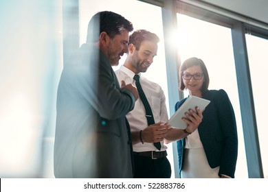 Group of businesspeople using a digital tablet together in front of office building windows overlooking the city - Shutterstock ID 522883786
