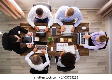 Group Of Businesspeople Working On Laptop Over Wooden Desk