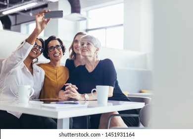 Group of businesswomen taking selfie at office cafeteria. Female business professionals taking selfie with smartphone during break in office. - Powered by Shutterstock