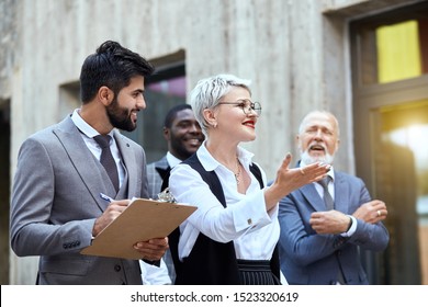 Group Of Busy Business People On The Move In Front Of The Office Building. Focus On Confident Young Man Walking Down The Street