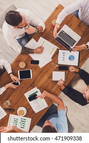 Group Of Busy Business People Working In Office, Top View Of Wooden Table With Mobile Phones, Laptop, Tablet And Documents Papers With Diagram. Men And Women Team Have Brainstorm Discussion, Vertical