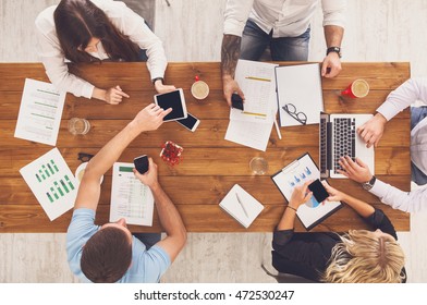 Group Of Busy Business People Working In Office, Top View Of Wooden Table With Mobile Phones, Laptop, Tablet And Documents Papers With Diagram. Men And Women Team Together Have Brainstorm Discussion.