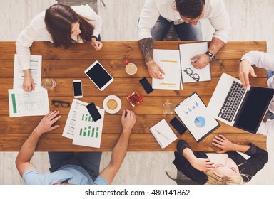 Group of busy business people working in office, top view of wooden table with mobile phones, laptop, tablet and documents papers with diagram. Men and women team together have brainstorm discussion. - Powered by Shutterstock