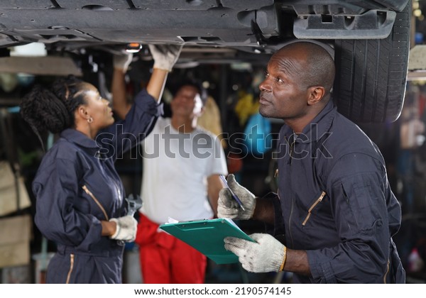 Group of car mechanic in uniform checking\
maintenance a lifted car service with clipboard at repair garage\
station. Worker holding wrench and fixing breakdown vehicle. Car\
repair service concept