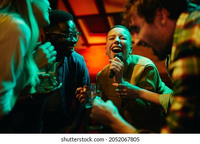 Group of carefree friends singing karaoke and having fun on night party in a bar. Focus is on black woman singing.
